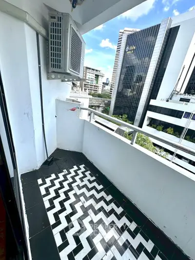 Chic urban balcony with stylish black and white tile flooring, offering a vibrant city view.