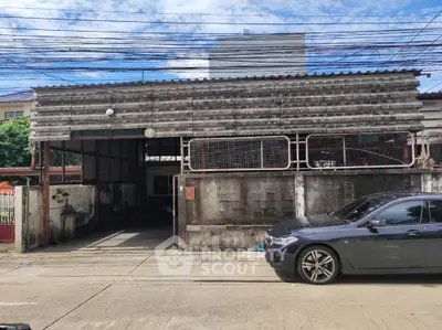 Industrial-style exterior with corrugated metal roofing and concrete walls, featuring a parked car in front.