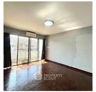 Spacious sunlit room with parquet flooring and large windows in modern apartment.