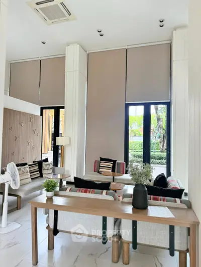 Spacious modern living room with high ceilings and stylish decor, featuring large windows and elegant furniture.
