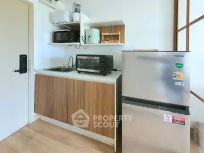 Modern compact kitchen with appliances including fridge, oven, and microwave in stylish apartment.
