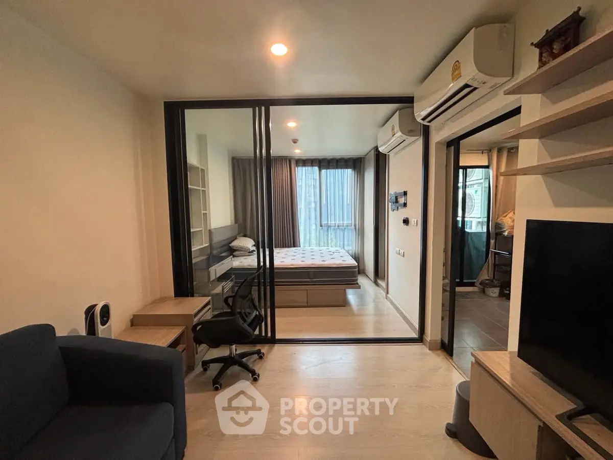 Modern apartment interior with cozy living room and stylish bedroom separated by glass partition.