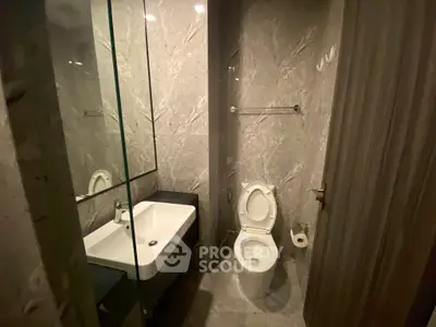 Modern bathroom with sleek design and marble tiles, featuring a toilet and sink.