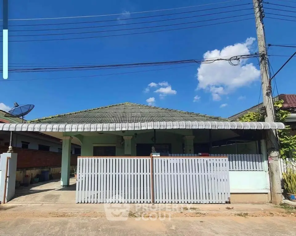 Charming single-story house with gated entrance and tiled roof under clear blue sky.