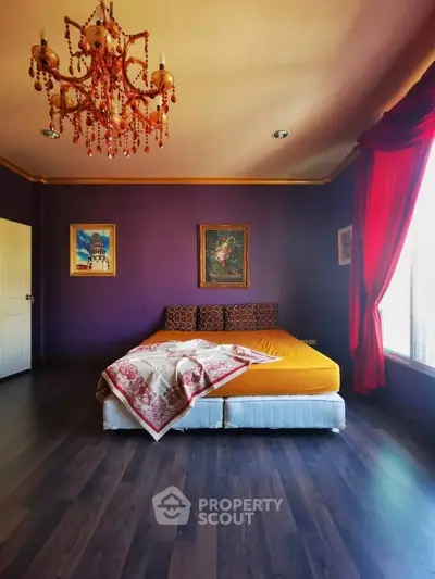 Luxurious bedroom with vibrant decor and elegant chandelier, featuring rich purple walls and large window.
