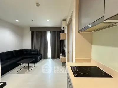 Modern living room with sleek kitchen, featuring black leather sofa and induction cooktop, perfect for urban living.