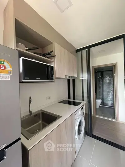 Modern compact kitchen with washing machine and microwave in sleek apartment.