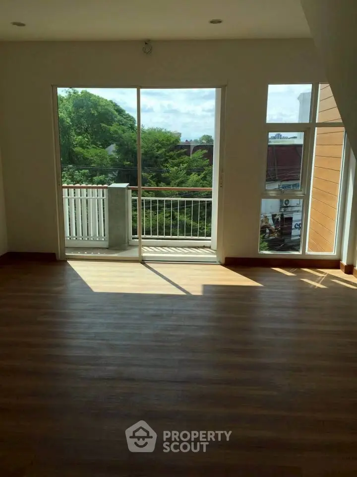 Spacious living room with large windows and balcony access, offering a serene view of lush greenery.