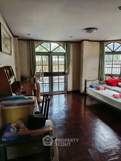 Spacious bedroom with wooden flooring and large windows offering natural light.