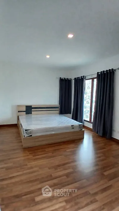 Spacious bedroom with wooden flooring and large windows for natural light.