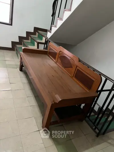 Wooden bench in a stairwell with tiled flooring, offering a cozy seating area in a residential building.