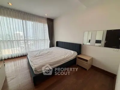 Spacious bedroom with large window and modern furnishings in a high-rise apartment.