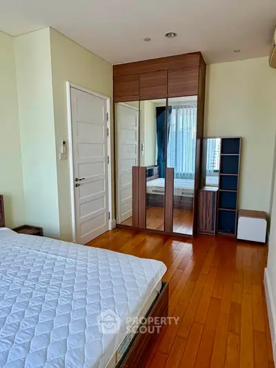 Spacious bedroom with wooden flooring and mirrored wardrobe in modern apartment