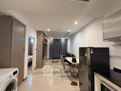 Modern apartment interior with sleek kitchen and cozy living area, featuring a washing machine and refrigerator.