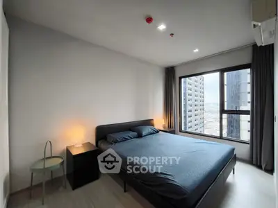 Modern bedroom with city view, featuring sleek furniture and large window for natural light.