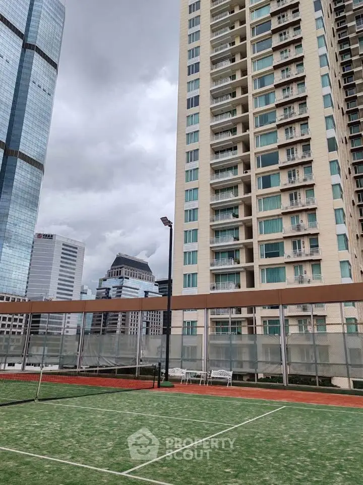 Luxurious high-rise building with tennis court and city skyline view.
