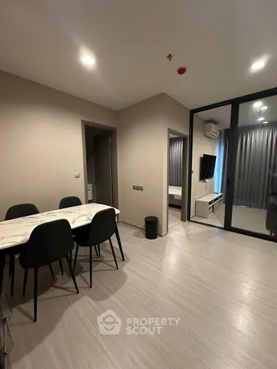 Modern apartment interior with dining area and view into bedroom, featuring sleek design and neutral tones.