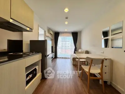 Modern open-layout living room with kitchen, featuring sleek furniture and large window for natural light.