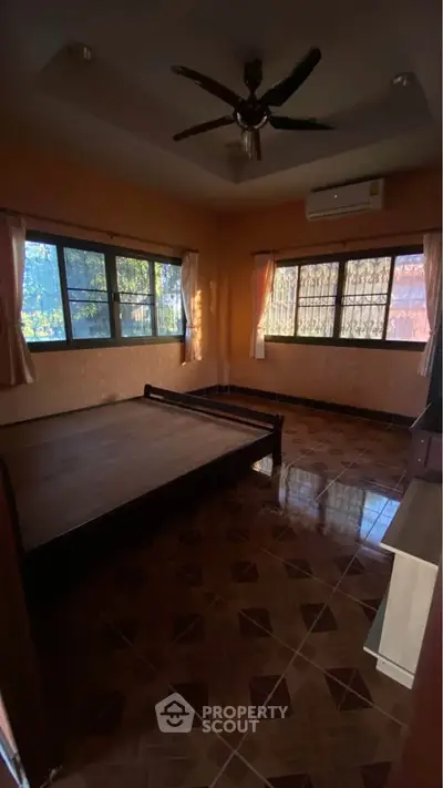 Spacious bedroom with large windows and ceiling fan, featuring warm lighting and tiled flooring.