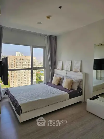Modern bedroom with large window offering stunning city views, featuring elegant decor and cozy bedding.