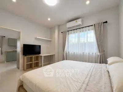 Spacious bedroom with modern decor and natural light, featuring a comfortable bed and a sleek TV setup.