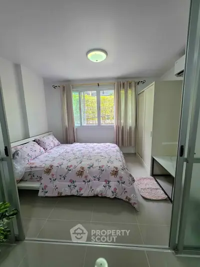 Cozy bedroom with floral bedding and ample natural light in modern apartment.
