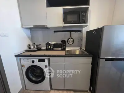 Modern compact kitchen with washing machine, microwave, and fridge in sleek apartment.