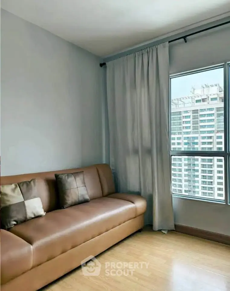 Modern living room with leather sofa and city view window in high-rise apartment.