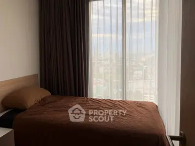 Cozy bedroom with city view through large window, featuring brown bedding and modern decor.