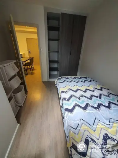 Cozy bedroom with modern laminate flooring leading to a well-lit dining area, featuring a large wardrobe and a view into the adjoining room.