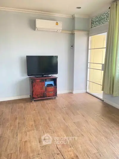 Spacious living room with wooden flooring and natural light, featuring air conditioning and a TV stand.