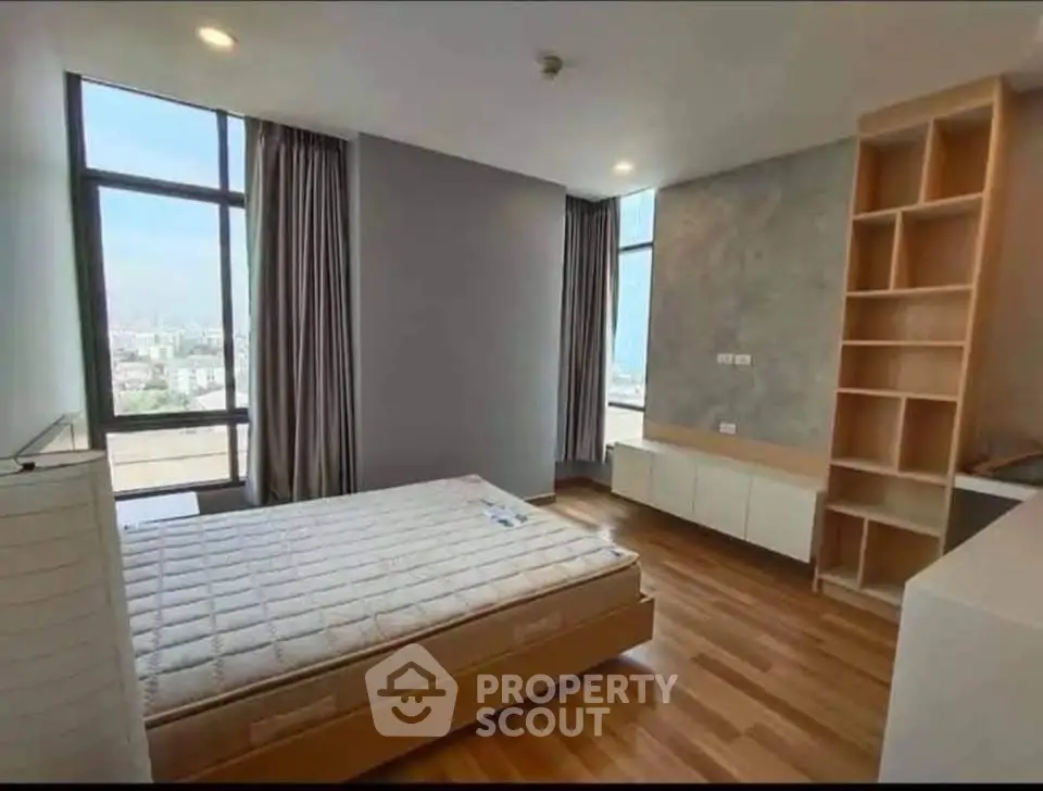 Spacious bedroom with large windows and wooden flooring offering city views.