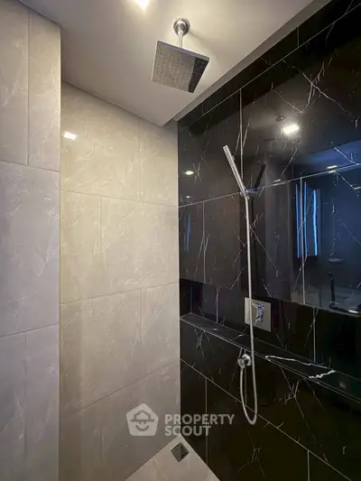 Luxurious modern bathroom with sleek black and marble tiles, featuring a rainfall showerhead.