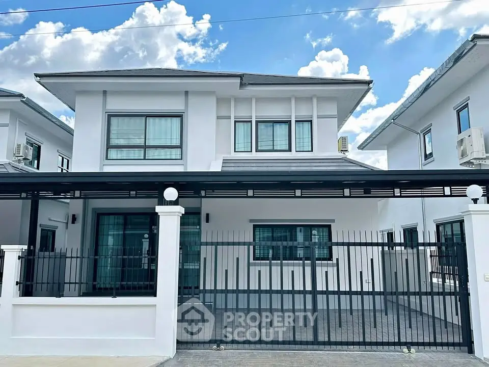 Modern two-story house with sleek design and gated entrance under a clear blue sky.