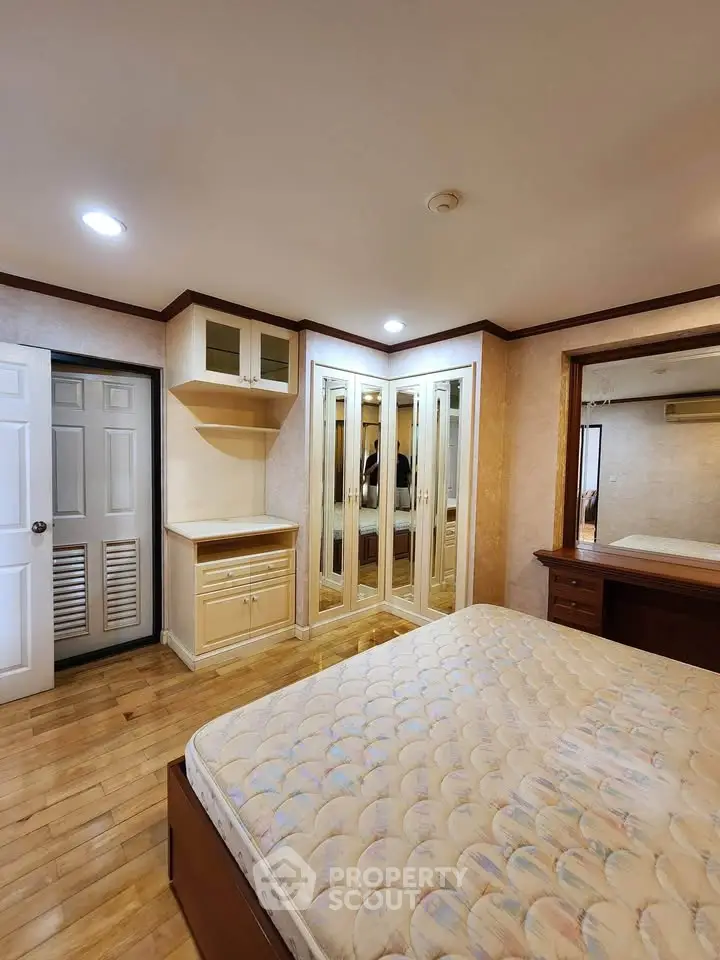 Spacious bedroom with wooden flooring and mirrored wardrobe in a cozy apartment.