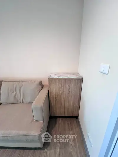 Modern living room corner with beige sofa and wooden cabinet on sleek flooring.