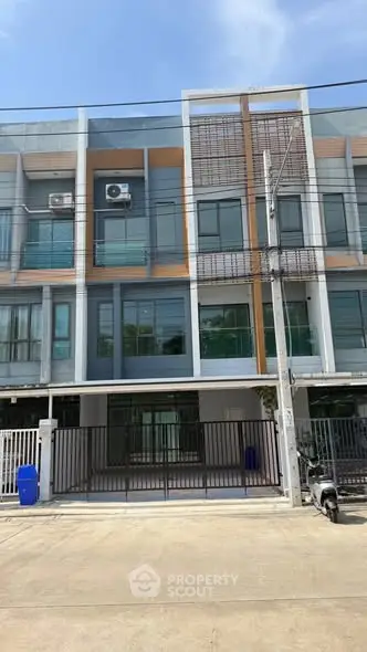 Modern three-story townhouse with sleek facade and gated entrance in urban setting.