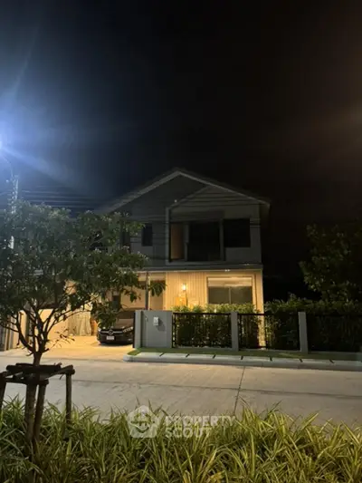 Modern two-story house with garage and garden at night, illuminated by streetlight.
