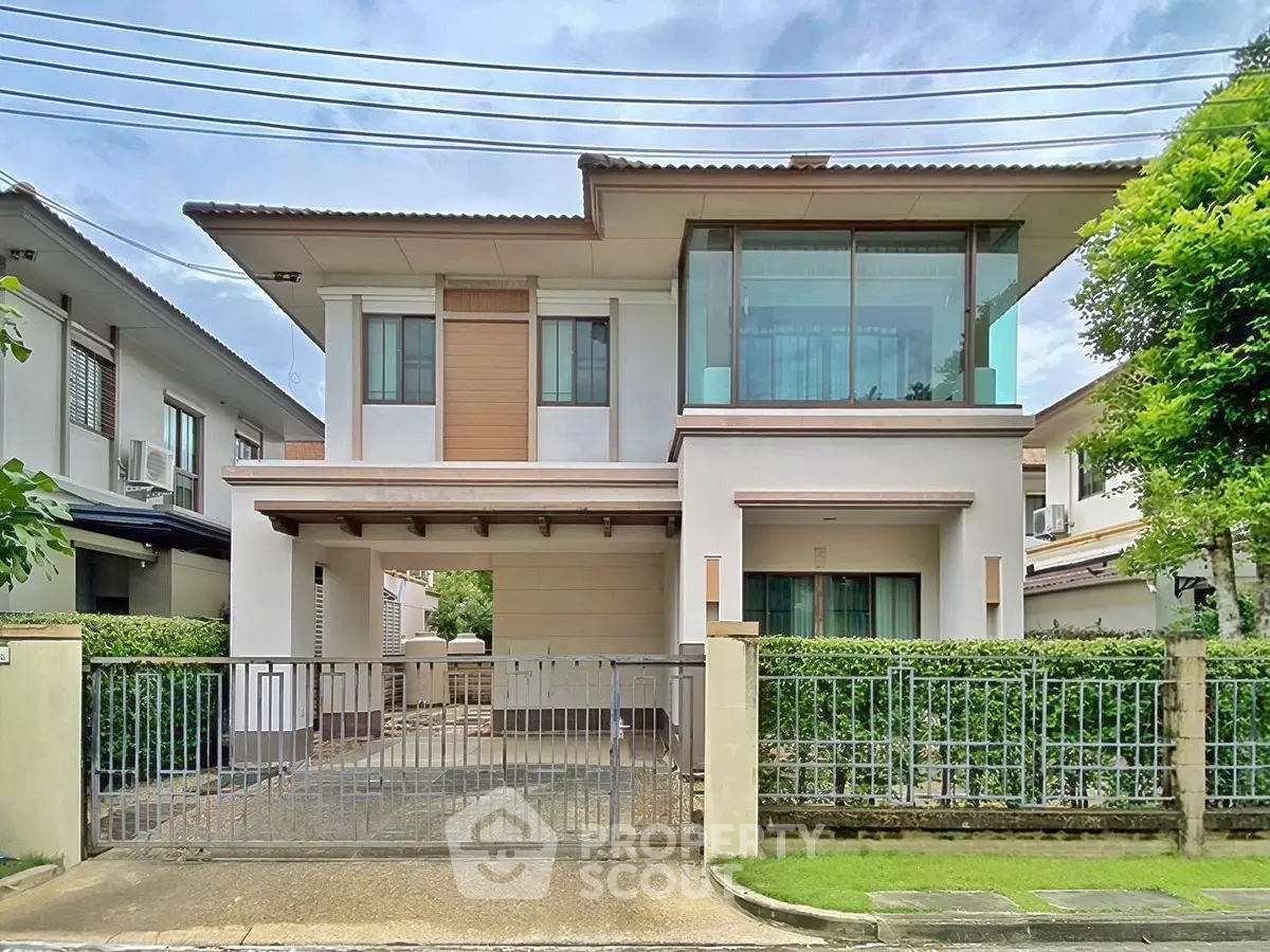 Modern two-story house with large windows and gated driveway in suburban neighborhood.