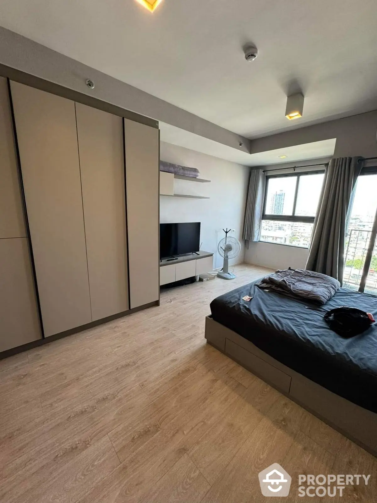 Modern bedroom with city view, featuring sleek wardrobe and cozy bed setup.