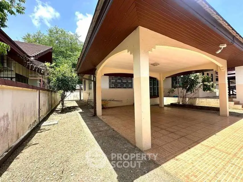 Spacious covered parking area in a suburban home with tiled flooring and lush greenery.