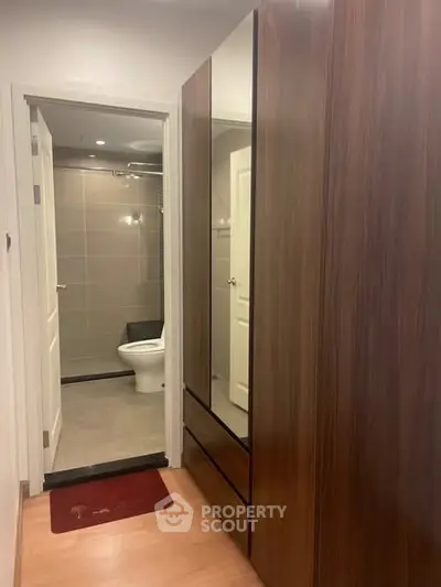 Modern apartment hallway leading to a sleek bathroom with wooden wardrobe and tiled flooring.