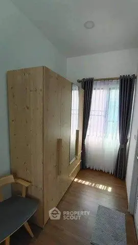 Cozy bedroom with wooden wardrobe and natural light through window.