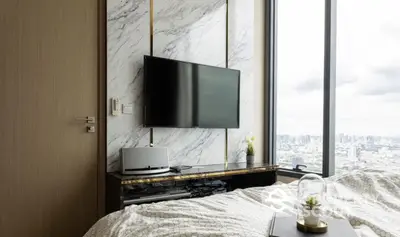 Modern bedroom with city view, featuring a wall-mounted TV and elegant decor.