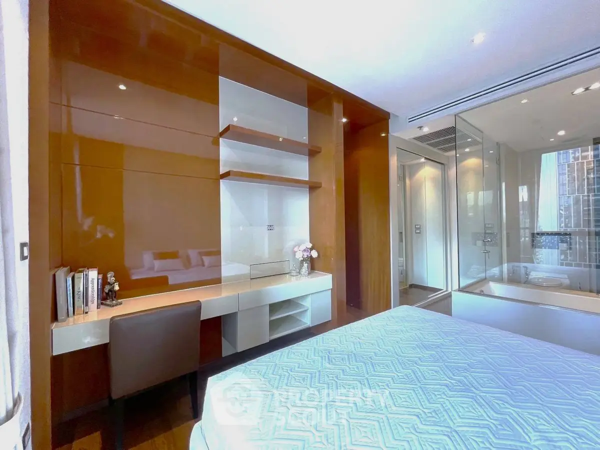 Luxurious bedroom with built-in study area and modern glass-enclosed bathroom, featuring elegant decor and ample natural light.