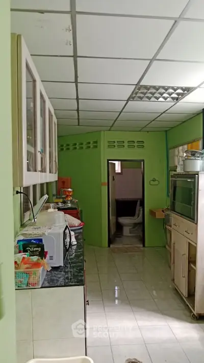 Cozy kitchen with closed layout and microwave, leading to a small bathroom.