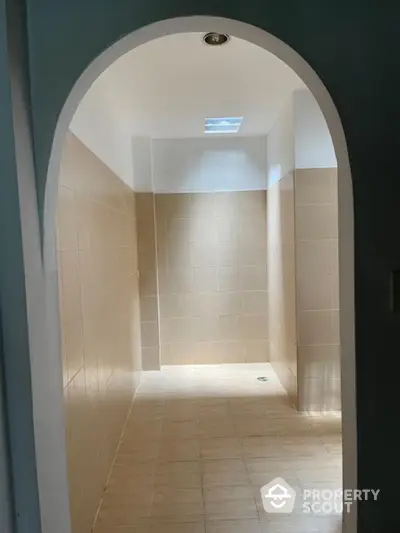 Spacious tiled bathroom with natural light and arched entrance