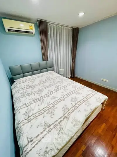 Cozy bedroom with wooden flooring and modern air conditioning unit, perfect for relaxation.