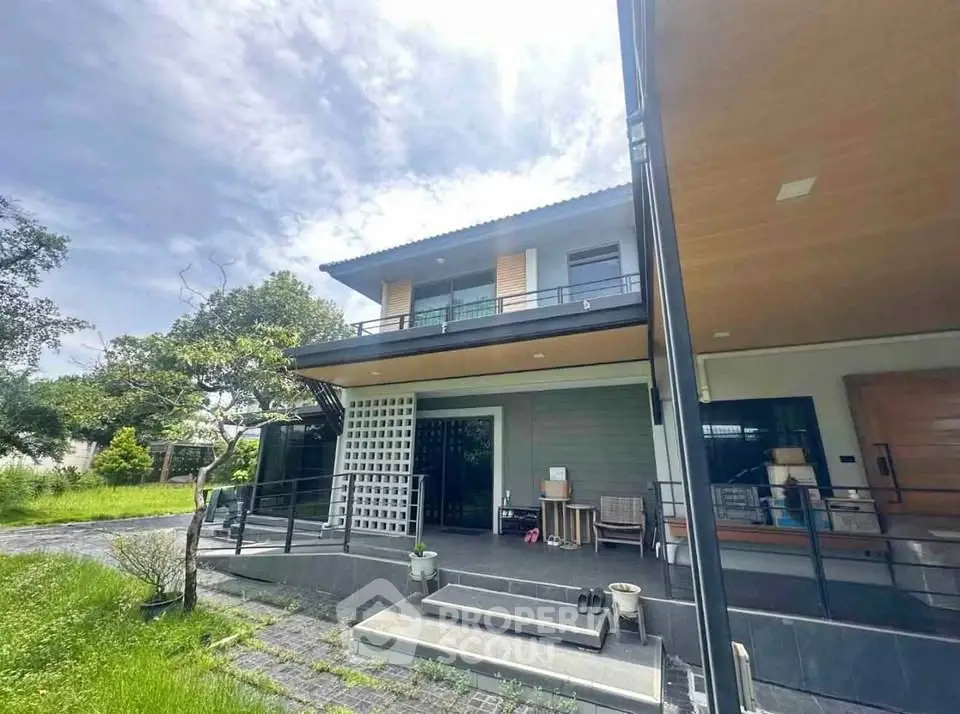 Modern two-story house with spacious balcony and lush green surroundings