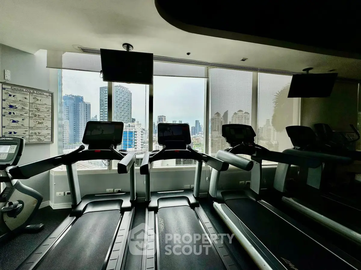Modern gym with city view featuring treadmills and large windows in a high-rise building.